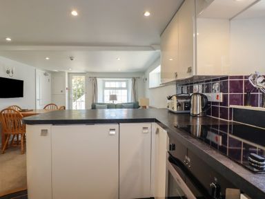 A kitchen with black countertop white cabinets toaster kettle and dining area with wooden chairs and table at St Saviours Padstow