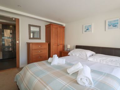 A bedroom with a double bed with white sheets and rolled towels a wooden chest of drawers and wardrobe a bedside table with a lamp and two framed pictures on the wall at St Saviours in Padstow