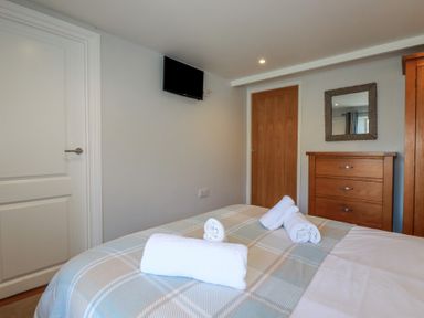 A bedroom with a bed with folded towels a wooden dresser a wall mirror and a wall mounted television at St Saviours in Padstow