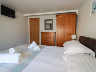 A bedroom with a bed with white sheets towels a wooden wardrobe and chest of drawers at St Saviours in Padstow