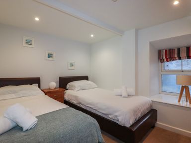 A bedroom with two single beds a bedside table with a lamp three pictures on the wall and a window with a striped blind at St Saviours in Padstow
