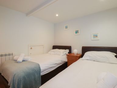 A bedroom with two single beds a wooden bedside table with a lamp and framed pictures on the wall at St Saviours in Padstow