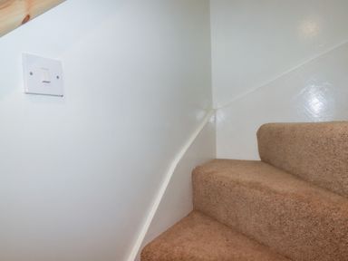 A carpeted staircase with white walls and a light switch at St Saviours in Padstow