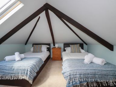 A bedroom with two single beds and a wooden nightstand under a slanted ceiling with exposed beams at St Saviours in Padstow
