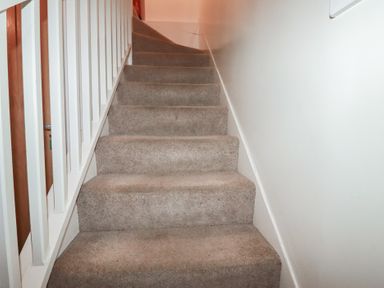 A carpeted staircase with white banisters and a plain wall at St Saviours in Padstow