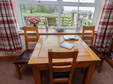A wooden dining table with three chairs in front of a window with red and beige plaid curtains at Folly View in Eglingham