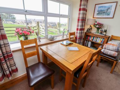 A dining area with a wooden table and four chairs near a window with decorative items and books at Folly View in Eglingham