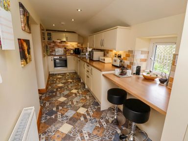 A kitchen with patterned floor tiles cream cabinets and a wooden countertop with two black bar stools at Folly View in Eglingham