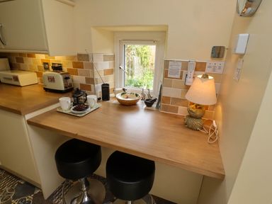 A kitchen counter with two black bar stools a lamp a toaster cups and a window at Folly View in Eglingham