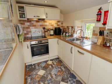 A kitchen with white cabinets, a built-in oven, a sink, a window, and kitchen utensils at Folly View in Eglingham