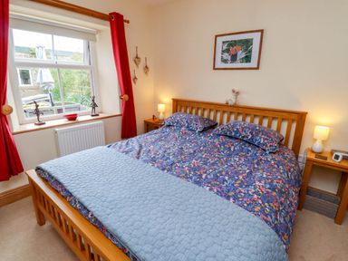 A bedroom with a wooden double bed with floral bedding and bedside tables with lamps at Folly View in Eglingham