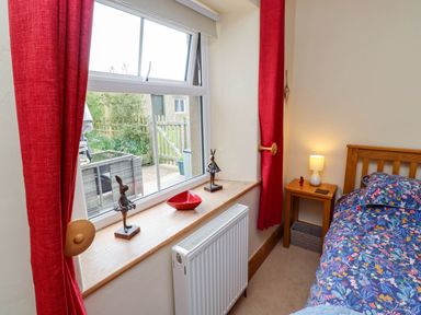 A bedroom window with red curtains two rabbit figurines and a red bowl on the windowsill beside a wooden bed and bedside table with a lamp at Folly View in Eglingham