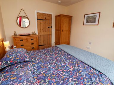 A bedroom with a wooden bed with floral bedding a wooden dresser with a mirror and a wooden wardrobe at Folly View in Eglingham