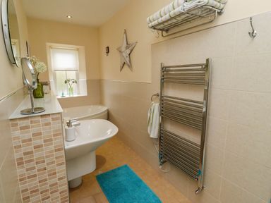 A bathroom with a white sink a bathtub a towel rack and a blue rug at Folly View in Eglingham