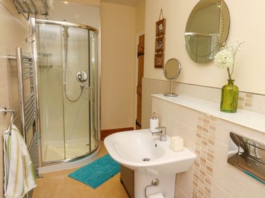 A bathroom with a corner shower, sink, round wall mirror, green vase with flowers, and a towel rack at Folly View in Eglingham