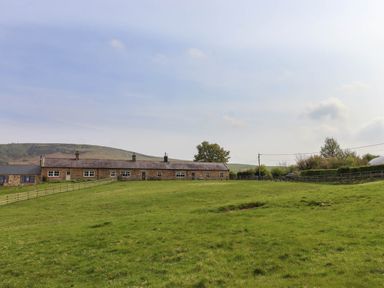 A grassy field with a fenced area and a row of stone buildings with doors and windows at Folly View in Eglingham