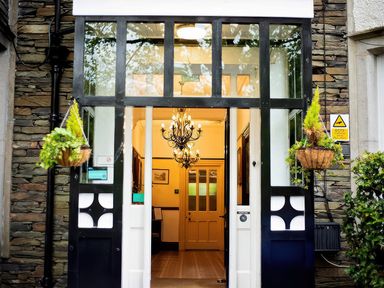 An entrance with black and white framed glass doors hanging plants and a chandelier inside at Fir Trees in Windermere