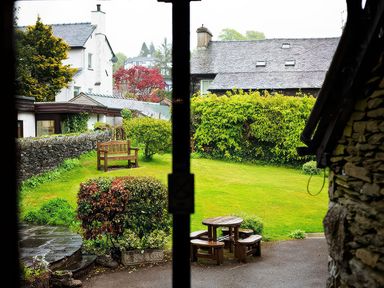 A garden with wooden bench and round wooden table with benches near a stone wall at Fir Trees in Windermere