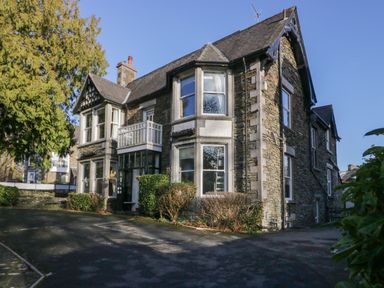 A stone house with multiple windows and a driveway with bushes at Fir Trees in Windermere