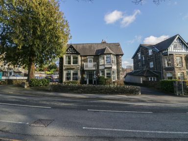 A street view of two stone houses with bay windows and a large tree at Fir Trees in Windermere