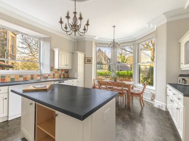 A kitchen with an island countertop dining table and chairs and large windows at Fir Trees in Windermere
