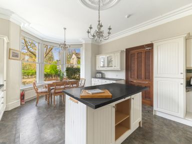 A kitchen with a central island and dining table by large windows at Fir Trees in Windermere