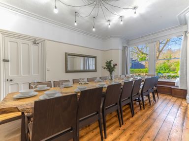 A dining room with a long wooden table surrounded by chairs and set with plates and glasses at Fir Trees in Windermere