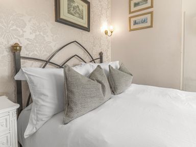 A bed with white sheets and three gray pillows against a floral wallpaper at Fir Trees in Windermere