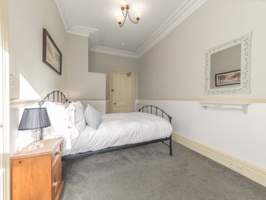 A bedroom with a single bed a wooden nightstand with a lamp a framed picture and a mirror on the walls at Fir Trees Windermere