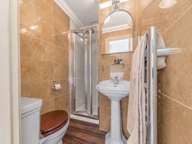 A bathroom with a toilet with wooden seat a pedestal sink a glass shower enclosure and a towel on a chrome rail at Fir Trees in Windermere