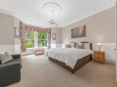 A bedroom with a bed two bedside tables with lamps a sofa and a window with curtains at Fir Trees in Windermere