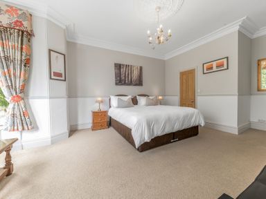 A bedroom with a double bed bedside tables lamps paintings and floral curtains at Fir Trees in Windermere