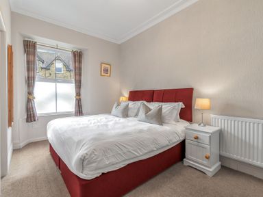 A bedroom with a double bed red headboard beside a nightstand and window at Fir Trees in Windermere
