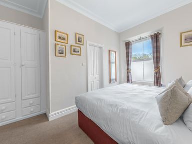 A bedroom with a bed near a window with curtains and framed pictures on the wall at Fir Trees in Windermere