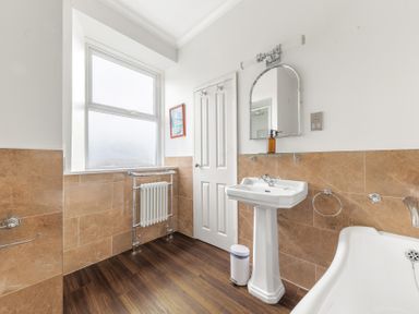 A bathroom with a pedestal sink mirror bathtub window and a radiator at Fir Trees in Windermere