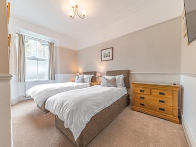 A bedroom with two single beds bedside tables lamps a window and a wooden chest of drawers at Fir Trees in Windermere
