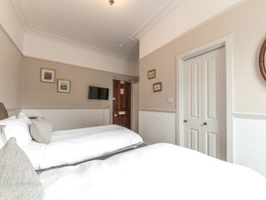 A bedroom with two beds pillows wall paintings a door and a television at Fir Trees in Windermere