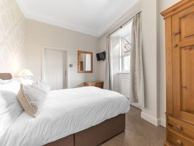 A bedroom with a bed pillows curtains wardrobe and a wall-mounted television at Fir Trees in Windermere