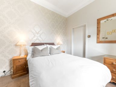 A bedroom with a double bed two bedside tables two lamps and a wall mirror at Fir Trees in Windermere