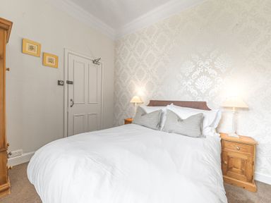 A bedroom with a double bed two bedside tables with lamps wooden wardrobe and decorative wallpaper at Fir Trees in Windermere
