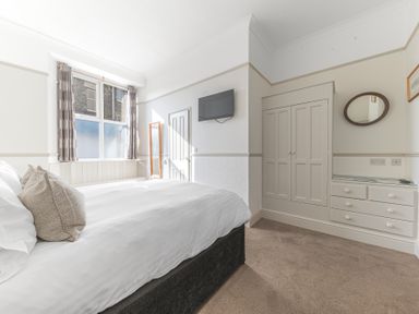 A bedroom with a bed pillows curtains a wall mounted TV a closet and a mirror at Fir Trees in Windermere