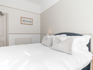 A bedroom with a double bed with white bedding and pillows a framed picture on the wall radiator and a closed door at Fir Trees in Windermere