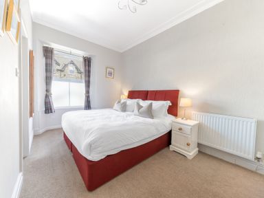 A bedroom with a red bed frame white bedding bedside table with lamp and window with curtains at Fir Trees in Windermere