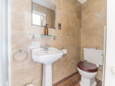 A bathroom with a pedestal sink a wall mirror and a toilet with a wooden seat at Fir Trees in Windermere