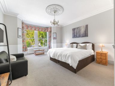 A bedroom with a bed bedside tables and lamps a sofa and a table near a window at Fir Trees in Windermere