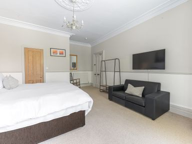 A bedroom with a bed a black sofa a wall mounted TV a wooden door and a chair at Fir Trees in Windermere