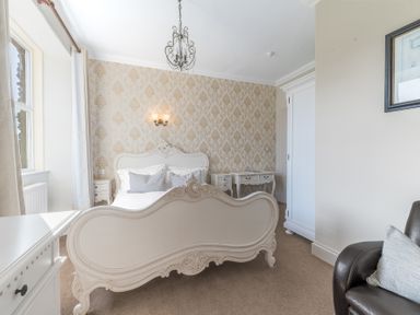 A bedroom with a white ornate bed a window with curtains a white wardrobe and a brown armchair at Fir Trees in Windermere