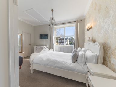 A bedroom with a white bed and bedside tables a window with curtains and a wall-mounted television at Fir Trees in Windermere