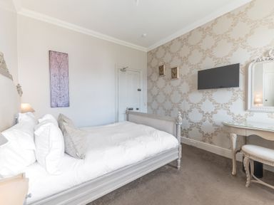 A bedroom with a bed white bedding a wall mounted television a dressing table and patterned wallpaper at Fir Trees in Windermere