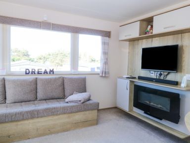 A seating area with a sofa under a large window and a wall-mounted television above an electric fireplace at 31A Foxburrow Hang in Fritton near Belton Norfolk